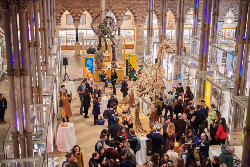 the arches and pilars of the Museum of Natural History surround the people celebrating the start of the MRC CoRE, among the exhibits, including skeletons of dinosaurs